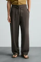 Pantalón marrón de corte ancho, con cintura ajustable con cordón, bolsillos delanteros y traseros tipo parche, detalle de costuras verticales en el frente y cierre frontal con cremallera y gancho metálico oculto.