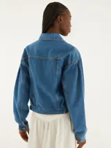 Chaqueta cropped de denim azul con mangas largas y cierre de botones. Tiene bolsillos con solapa y corte recto.