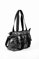 Cartera tipo tote bag color gris oscuro brillante, con diseño acolchado y correas de tela negras. Incluye dos correas frontales decorativas con hebillas de plástico negras y una correa lateral ajustable.