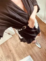 Cinturón de cuero negro con hebilla plateada y riñonera plateada con flecos.