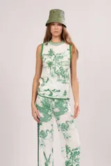 Musculosa blanca con estampado de palmeras, camellos y aves en color verde. Tiene cuello redondo y ribete verde en cuello y sisas.