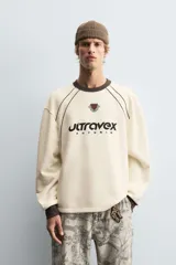 Sudadera color crema de corte relaxed fit, con cuello redondo y manga larga. Presenta un estampado en el frente con la palabra "ULTRAVEX" en letras negras y la palabra "FUTURIO" debajo.