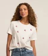 Remera t-shirt blanca de algodón con cuello redondo y mangas cortas. Presenta bordados de cerezas rojas dispersos en el frente.