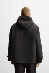 Parka negra de corte regular, confeccionada en tejido técnico acolchado. Tiene cuello alto con capucha ajustable, mangas largas con puños ajustables, bolsillos con solapa en la cadera y un bolsillo interior. El cierre frontal es con cremallera oculta por solapa con botones a presión.