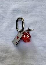 Llavero colgante con mosquetón metálico plateado, dije de naipe As de corazones, dije de estrella plateada, dije de corazón con inscripción "made with love" y dado rojo translúcido.