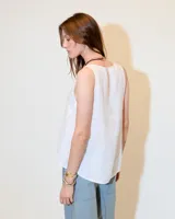 Top sin mangas blanco de lino, con escote redondo, corte en A, ruedo asimétrico y recortes laterales.
