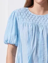 Blusa celeste de gasa marca Zac & Rachel, con cuello redondo, frunces en el frente, mangas 3/4 con puño, abertura central en la espalda y botón.