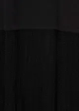 Vestido negro de punto ajustado al cuerpo, sin mangas y con cuello alto. Largo hasta la rodilla y ruedo con flecos.