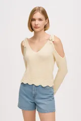 Sweater de punto color crema, con escote en V, hombros descubiertos y mangas largas. Presenta detalle de lazos en los hombros y terminación ondulada en el ruedo.
