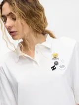 Remera tipo polo blanca de manga corta con hombreras y pins removibles en la delantera.