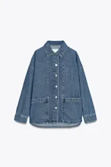 Sobrecamisa de denim azul de Zara Woman Collection, confeccionada en algodón 100%. Tiene cuello solapa, manga larga con puños, bolsillos de plastrón en el delantero y cierre frontal con botones metálicos.