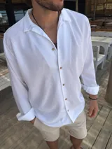 Camisa blanca de fibrana con cuello clásico, manga larga con puños arremangados y cierre frontal con botones de madera.
