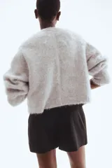 Short pollera negro de tiro alto con diseño cruzado tipo pareo en el frente, asegurado con un cinturón cosido y hebilla revestida. Presenta cierre oculto y cierre de corchete en un lateral.