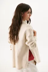 Sobrecamisa color beige de lino con cuello camisero, cierre frontal con botones negros, mangas largas con puños abotonados, dos bolsillos de parche en el pecho y dos bolsillos laterales.