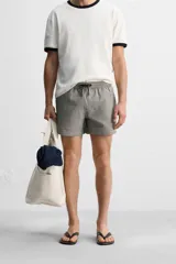 Short de baño con textura seersucker a rayas verticales azul marino y blanco. Tiene cintura elástica ajustable con cordón, bolsillos frontales y traseros, aberturas laterales en el bajo y forro interior.