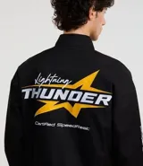 Campera negra con cuello alto, cierre de botones y estampado estilo racing con logos y textos en amarillo, rojo y blanco. Tiene bolsillos laterales y mangas largas con detalles estampados. Marca Blue Steel.