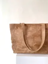 Cartera tipo tote de cuero graneado color negro, con textura uniforme y suave al tacto. Tiene manijas de 55 cm, bolsillo frontal con broche imantado, bolsillo trasero con cierre metálico, cierre principal metálico, forro interior y tres bolsillos internos (uno con cierre, uno plaqué y uno tipo sobre con solapa y botón).