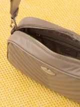 Bandolera color beige con diseño acolchado en forma de V y logo metálico dorado en forma de labios. Tiene correa larga ajustable y herrajes plateados.