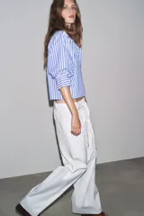 Camisa de cuello redondo con estampado de rayas verticales azules y blancas, manga larga abullonada y cierre frontal con botones.