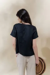 Blusa de lino color beige con rayas verticales negras, corte recto, escote redondo y mangas cortas.