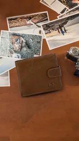 Billetera de cuero marrón con presilla y broche a presión. Cuenta con doble repartición para billetes, tarjeteros, bolsillos y monedero con cierre. Tiene las iniciales "LNS" grabadas en el frente.