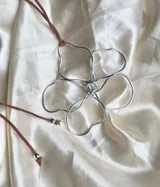 Collar con colgante de flor de cinco pétalos hecha de alambre plateado y cordón marrón ajustable.