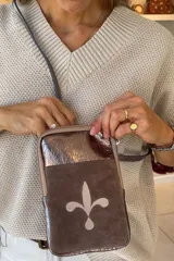 Bandolera pequeña de cuero color marrón con aplique de cuero brillante en la parte superior y un diseño bordado con forma de flor de lis en la parte inferior.