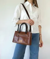 Cartera bandolera de cuero color marrón tostado, con doble asa corta y correa larga desmontable. Tiene un bolsillo frontal con cierre y un bolsillo interno.