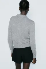 Chaqueta de punto gris con cuello solapa y manga larga. Tiene bolsillos delanteros de plastrón, rib en los acabados y cierre frontal con botones a presión en forma de lazo.