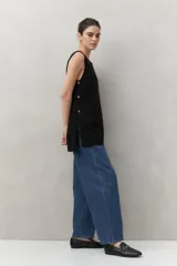 Blusa sin mangas negra de punto suave y fluido, con silueta larga y recta. Presenta botones dorados en los laterales.