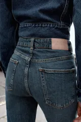 Pantalón de jean azul de tiro alto, corte mom fit, tobillero y con cinco bolsillos. Cierre frontal con cremallera y botón.