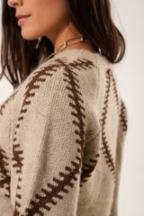 Sweater beige de punto con cuello redondo y manga larga. Presenta un diseño geométrico en color marrón.