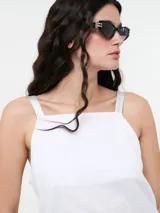 Top blanco de lino con escote recto y breteles de cuero sintético. El largo de esta prenda es irregular, siendo más larga la pieza de la espalda.