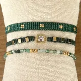 Set de tres pulseras elásticas con cuentas de ágata musgo y acero, pulsera tejida con cuentas Miyuki en tonos de verde y dorado, y pulsera tejida con dije de acero con cristal y cuentas cubo de hematita.