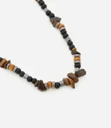 Collar corto con cuentas de piedra color marrón, cuentas de madera color beige, cuentas metálicas color gris y cuentas de madera color negro.