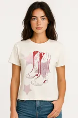 Remera color crema de algodón con cuello redondo y mangas cortas. Estampado frontal de dos botas de cowboy rojas con estrellas rosas.
