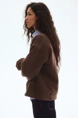 Buzo de tejido de punto color marrón oscuro, con cuello redondo, hombros caídos y puños y bajo acanalados. Presenta un estampado frontal en color crema con el texto "CHARME DE PARIS 1998".