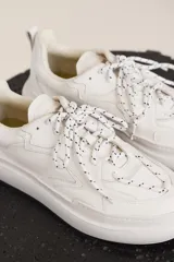 Zapatillas urbanas blancas de cuero con cordones moteados en blanco y negro y suela chunky.