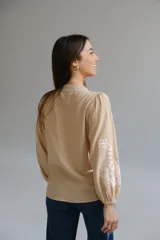 Camisa color beige con bordados florales blancos, cuello mao, mangas largas con elástico en los puños y cierre frontal con botones.