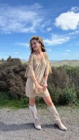Vestido corto color beige, con escote en V con cordones, mangas 3/4 acampanadas con cordones y hombros descubiertos.