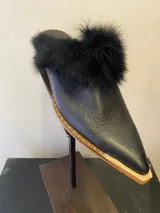 Mules de cuero negro con punta fina, detalle de tachas doradas en la suela y adorno de piel sintética en el empeine.