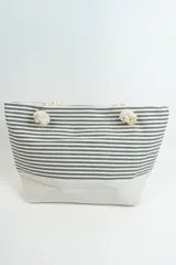 Bolso tipo tote con base color crema y cuerpo a rayas horizontales grises y blancas. Asas de soga con nudos.