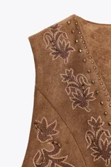 Chaleco marrón de efecto ante con bordados florales y abalorios. Tiene escote en pico, sin mangas y cierre frontal con lazada.