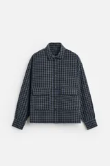 Camisa de hombre a cuadros azules y negros, de corte cuadrado, con cuello solapa, manga larga con puños abotonados, cierre frontal con botones y bolsillos de parche con solapa en el pecho.
