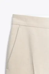Pantalón negro tobillero de tiro alto con bolsillos delanteros y traseros. Tiene abertura lateral en el bajo y cierre frontal con cremallera y botón.