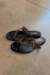 Sandalias negras con tiras finas marrones decoradas con tachas doradas.