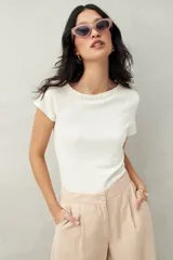 Top tejido color crudo, de silueta ajustada con diseño minimalista y escote redondo, adornado con pequeños botones metálicos.