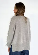 Sweater beige de tejido de punto con detalle de flecos en hombros y mangas.