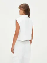 Chaleco corto color blanco, con cuello camisero, sin mangas y con bolsillos frontales.