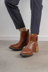Bota corta de cuero marrón con puntera redondeada y taco cuadrado. Presenta una correa con hebilla alrededor del tobillo y cierre lateral.